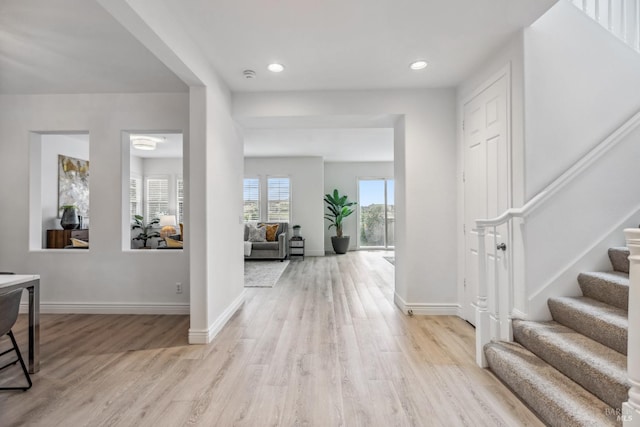 foyer with baseboards, stairs, and light wood-style flooring
