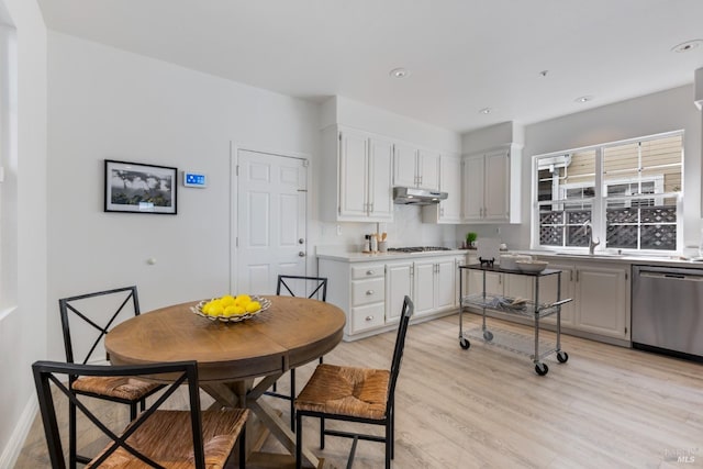 kitchen with a sink, dishwasher, white cabinetry, light wood-style flooring, and under cabinet range hood
