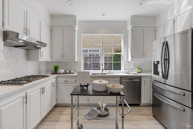 kitchen featuring under cabinet range hood, stainless steel appliances, a sink, light wood-style flooring, and white cabinetry