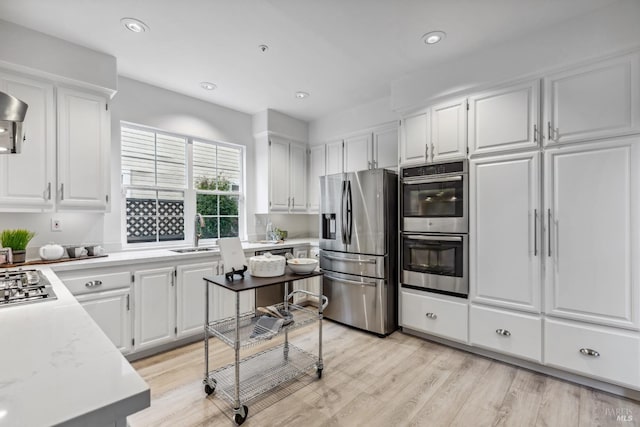 kitchen with white cabinets, appliances with stainless steel finishes, a sink, and light countertops