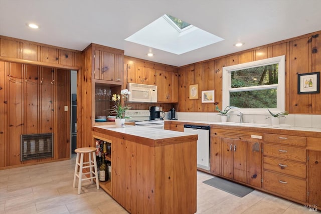 kitchen featuring tile counters, a skylight, heating unit, white appliances, and a sink