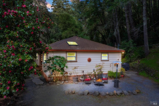 property exterior at dusk with roof with shingles and an outdoor fire pit