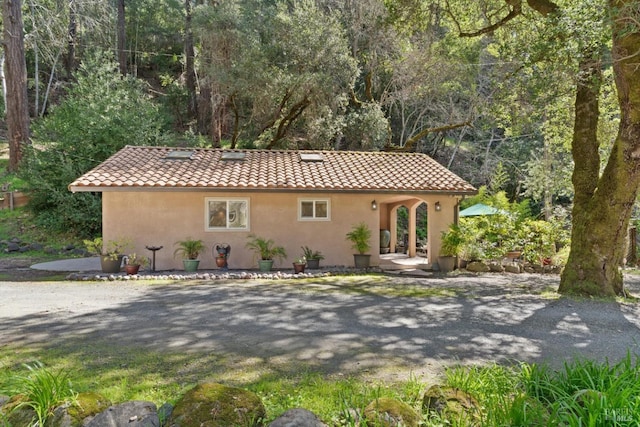 mediterranean / spanish-style house featuring stucco siding, a tile roof, and a view of trees