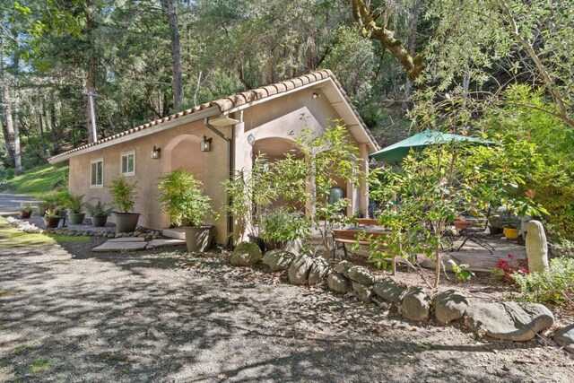exterior space featuring a tile roof, a view of trees, and stucco siding