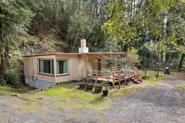 view of front of property with a chimney, a wooden deck, and a view of trees