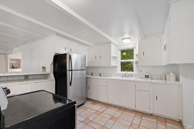 kitchen featuring black range with electric cooktop, tile countertops, decorative backsplash, freestanding refrigerator, and a sink