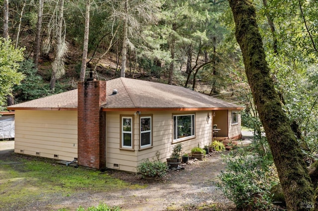 view of side of home featuring crawl space, a view of trees, a chimney, and a shingled roof