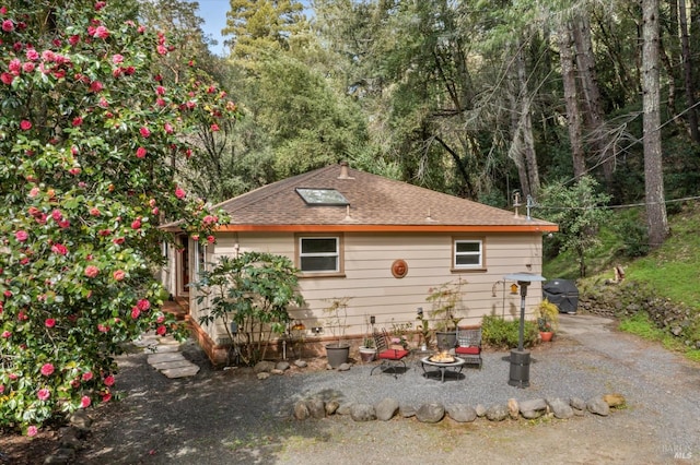 view of side of property featuring an outdoor fire pit and a shingled roof