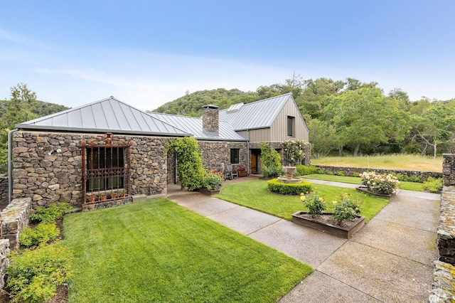 view of front facade with a standing seam roof, a front lawn, metal roof, stone siding, and a chimney