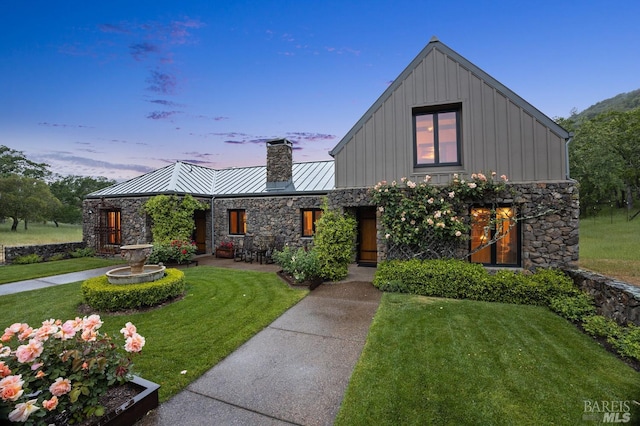 view of front of home with a standing seam roof, a yard, stone siding, board and batten siding, and a chimney