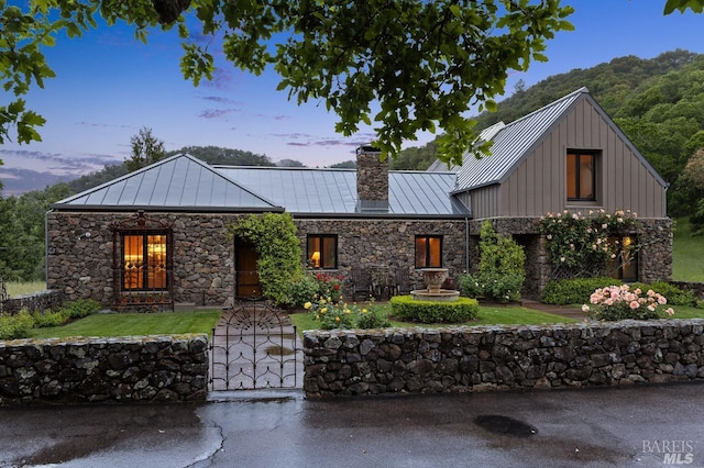 view of front of home featuring a standing seam roof, metal roof, stone siding, board and batten siding, and a chimney