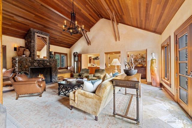 living room featuring a notable chandelier, high vaulted ceiling, a stone fireplace, and wooden ceiling