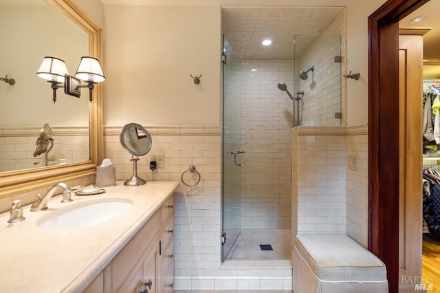bathroom with tile walls, a wainscoted wall, a shower stall, and vanity