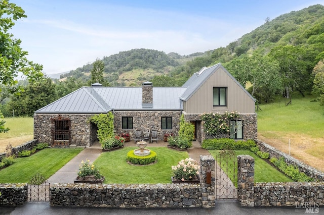 view of front of home with a front lawn, a standing seam roof, a gate, stone siding, and a chimney