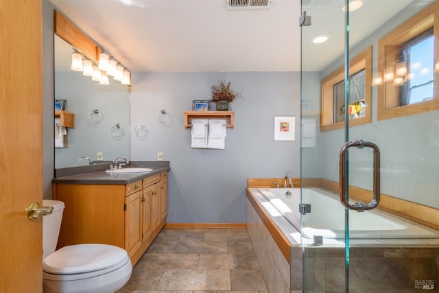 bathroom featuring stone finish flooring, baseboards, toilet, vanity, and a garden tub