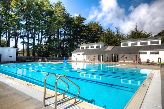 community pool with an outbuilding, fence, and a patio area