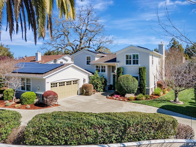 traditional-style house featuring a chimney, stucco siding, roof mounted solar panels, driveway, and an attached garage