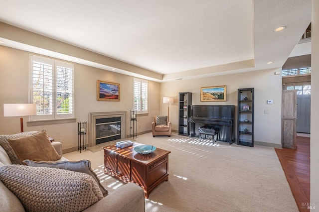 living room featuring baseboards, recessed lighting, a tray ceiling, and a glass covered fireplace