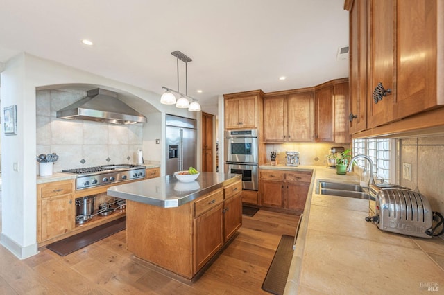 kitchen with stainless steel appliances, a kitchen island, backsplash, a sink, and wall chimney exhaust hood