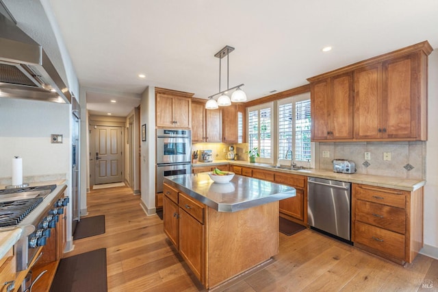 kitchen with wall chimney range hood, a sink, stainless steel appliances, a center island, and backsplash