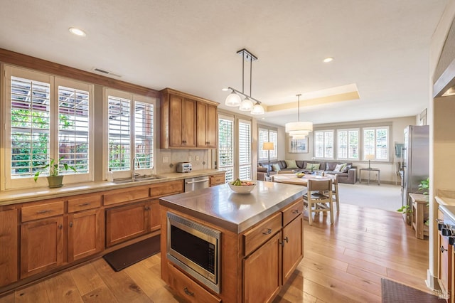 kitchen with a sink, stainless steel appliances, light wood-style floors, brown cabinetry, and open floor plan