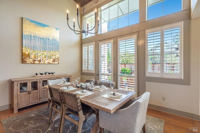dining room with baseboards, wood finished floors, an inviting chandelier, and a high ceiling