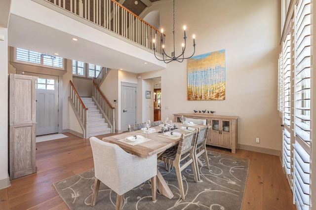dining room with hardwood / wood-style floors, baseboards, a towering ceiling, a notable chandelier, and stairs