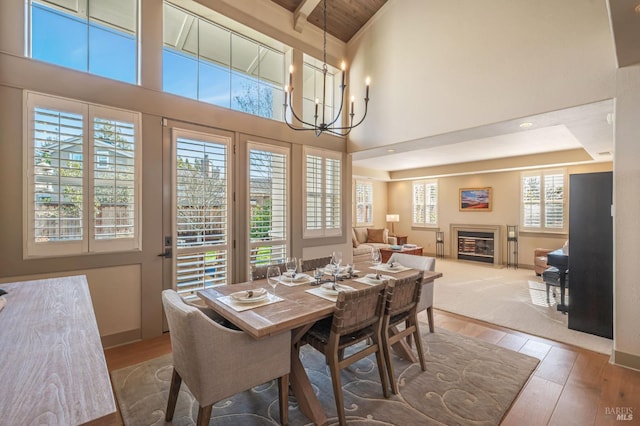 dining area featuring a high ceiling, a chandelier, wood finished floors, and a glass covered fireplace