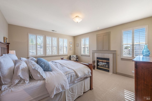 bedroom featuring a tile fireplace, visible vents, light colored carpet, and multiple windows
