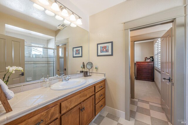 bathroom featuring tile patterned floors, vanity, baseboards, visible vents, and a stall shower