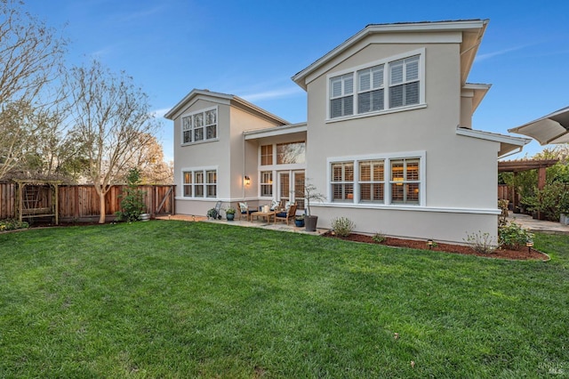 rear view of property featuring a lawn, stucco siding, a fenced backyard, and a patio area