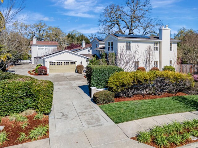 view of front of house featuring a garage, driveway, a chimney, roof mounted solar panels, and stucco siding