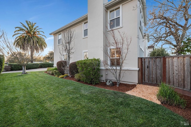 view of side of property featuring a yard, stucco siding, and fence