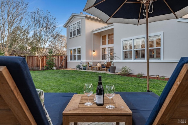 rear view of house featuring a patio, outdoor dining area, a lawn, stucco siding, and fence