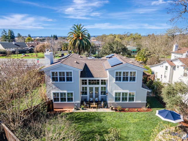back of property featuring a chimney, stucco siding, solar panels, a patio area, and a lawn