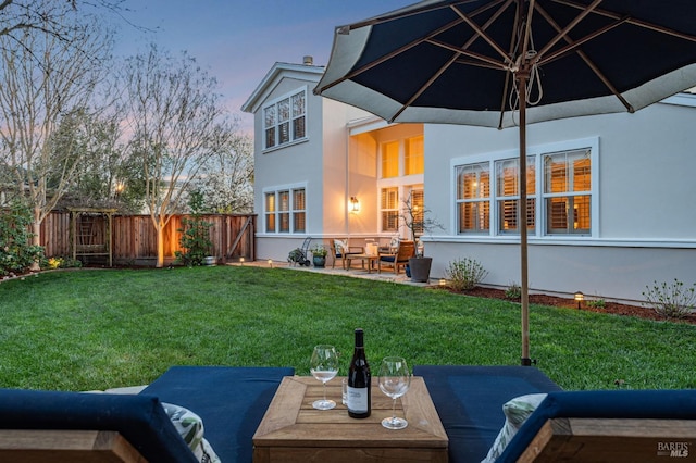 back of property at dusk featuring fence, a patio area, a yard, and stucco siding