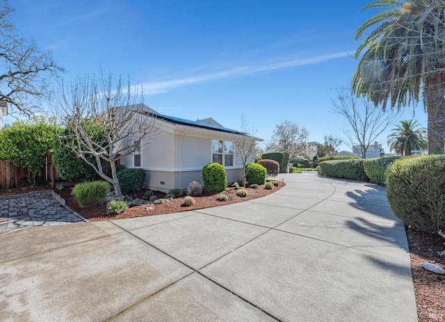 view of side of home featuring roof mounted solar panels, driveway, and fence