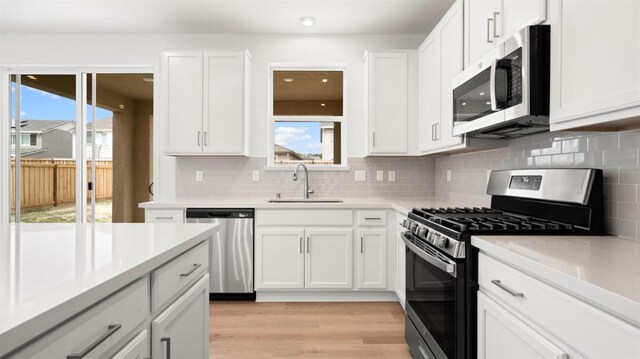 kitchen with decorative backsplash, stainless steel appliances, light countertops, white cabinets, and a sink