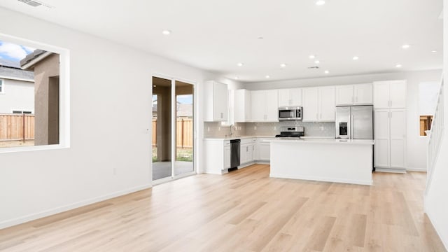 kitchen with decorative backsplash, white cabinetry, light wood-style flooring, light countertops, and appliances with stainless steel finishes