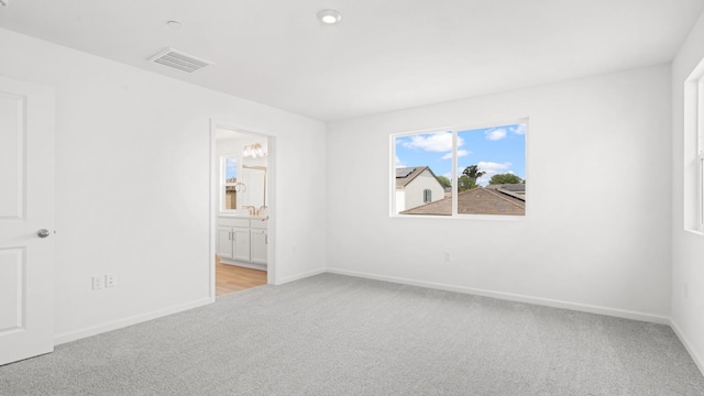 unfurnished bedroom featuring an inviting chandelier, connected bathroom, light carpet, baseboards, and visible vents