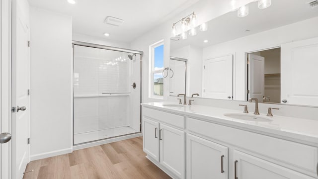 bathroom with a stall shower, wood finished floors, double vanity, and a sink
