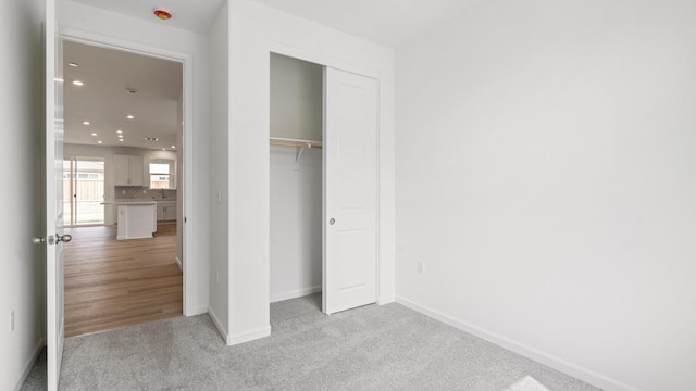 unfurnished bedroom with baseboards, recessed lighting, a closet, and light colored carpet
