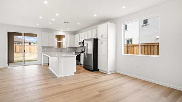 kitchen featuring white cabinets, a sink, appliances with stainless steel finishes, light countertops, and a kitchen island