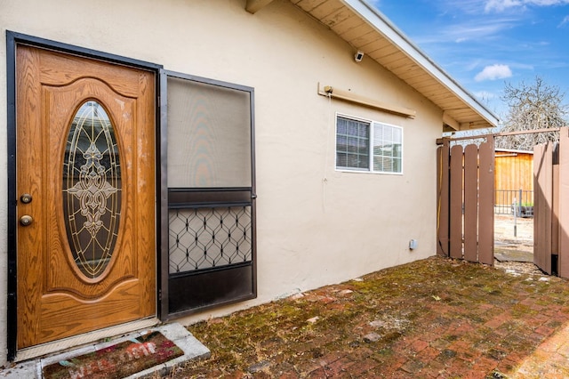 entrance to property featuring stucco siding and fence
