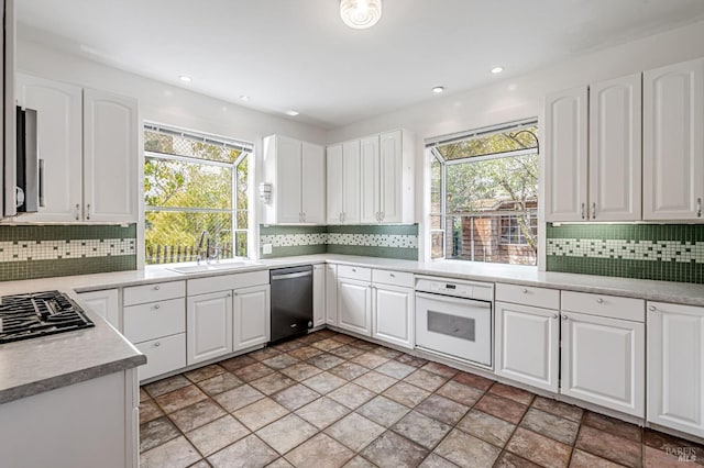 kitchen featuring stainless steel dishwasher, white oven, tasteful backsplash, and a sink
