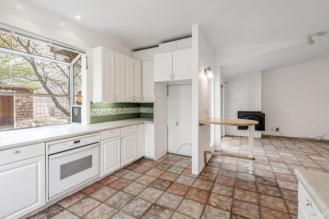 kitchen with light countertops, decorative backsplash, white oven, stone finish floor, and white cabinetry