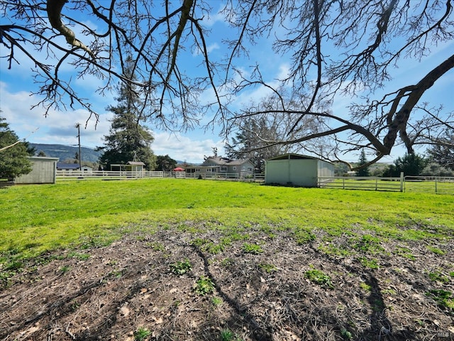 view of yard featuring a rural view, an outdoor structure, and fence