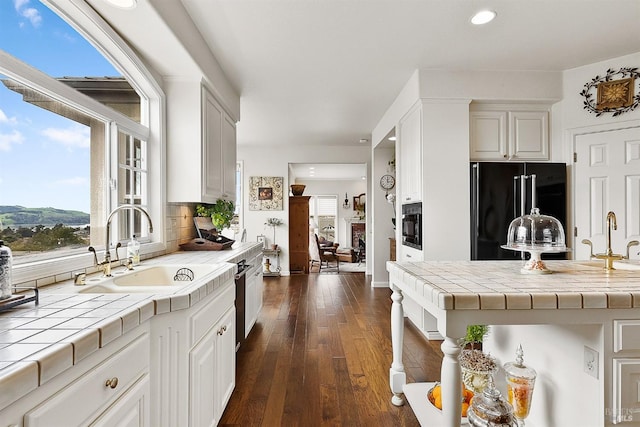 kitchen featuring black appliances, a healthy amount of sunlight, tile counters, and a sink
