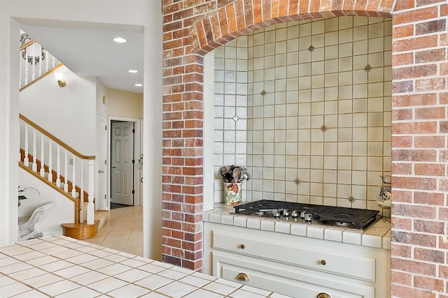 kitchen with stainless steel gas stovetop, decorative backsplash, tile counters, white cabinetry, and light tile patterned flooring
