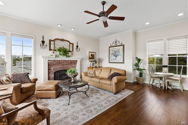 living room featuring baseboards, a brick fireplace, dark wood-style floors, a ceiling fan, and crown molding